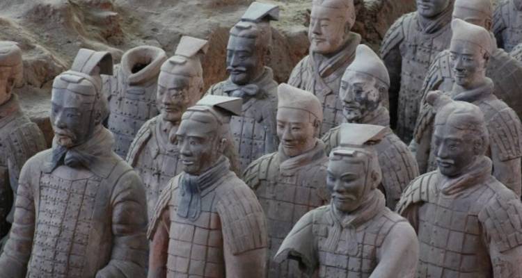 Row of life-sized Terracotta Warriors standing in excavated pit with detailed armor and faces.
