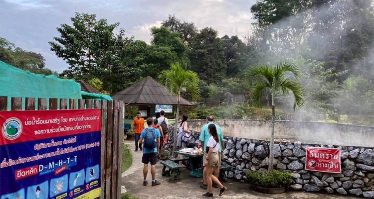 Los visitantes exploran una zona rural tailandesa de aguas termales con vapor que se eleva junto a la vegetación del bosque.