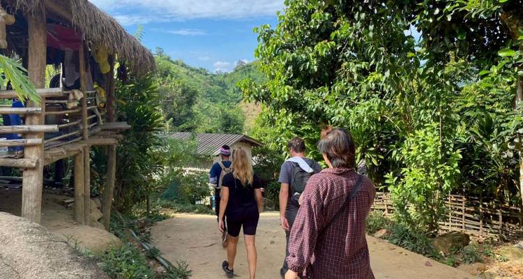 Los mochileros caminan por un sendero de tierra entre exuberantes jardines del pueblo y árboles de la selva.