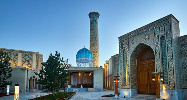 Elegante mausoleo con cúpula azul acanalada y alto minarete iluminado con suave luz vespertina.