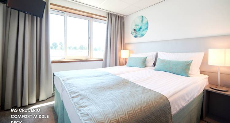 Helle, moderne Kreuzfahrtschiffkabine mit einem ordentlich gemachten Doppelbett, großem Fenster und sanfter grau-türkisfarbener Einrichtung.