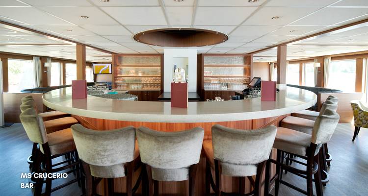 Geschwungene Flusskreuzfahrt-Bar mit hohen Hockern, Holzverkleidungen und hinterleuchteten Regalen.