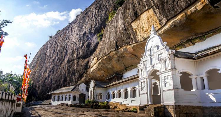 White rock-temple buildings built into cliff face under bright sky at Dambulla.