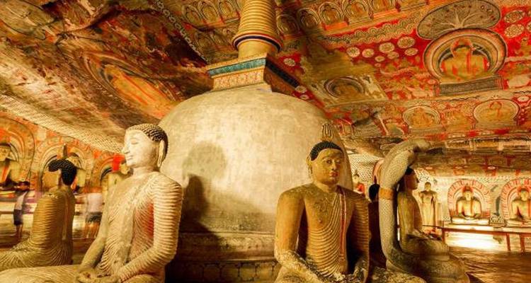 Interior of cave temple with Buddhas and painted ceilings illuminated by warm light.