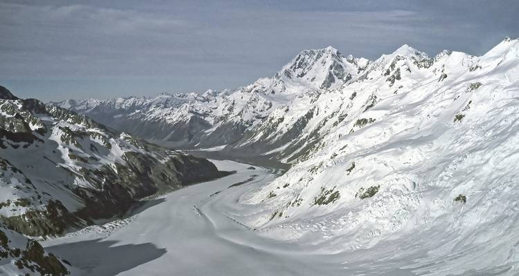 Une vue aérienne panoramique d'une vallée glaciaire enneigée encadrée par les pics accidentés des Alpes du Sud.