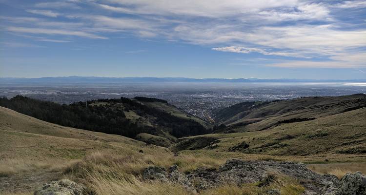 Une vue panoramique sur la ville de Christchurch depuis les collines herbeuses avec les Alpes du Sud faiblement visibles à l'horizon.