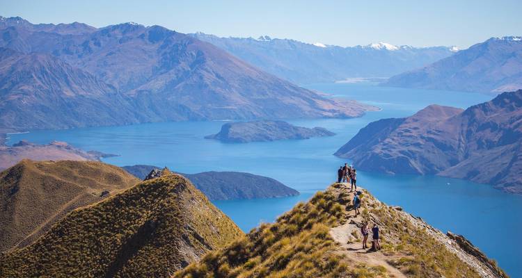Les randonneurs marchent sur une crête étroite vers le pic Roys surplombant l'étendue bleue du lac Wanaka et les chaînes enneigées.