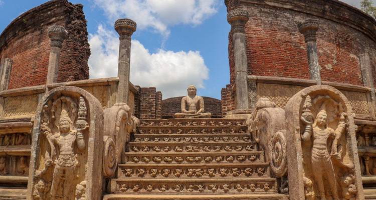 Stone stairway with intricate guard figures leading to a seated Buddha amid ancient brick ruins.