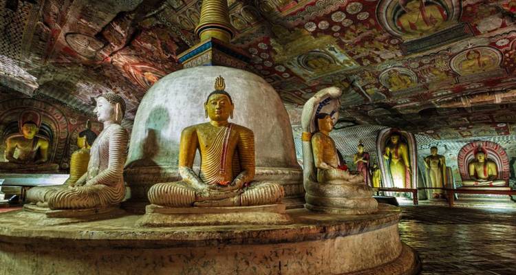 Interior of Dambulla Cave Temple with richly painted ceiling and golden Buddha statues.