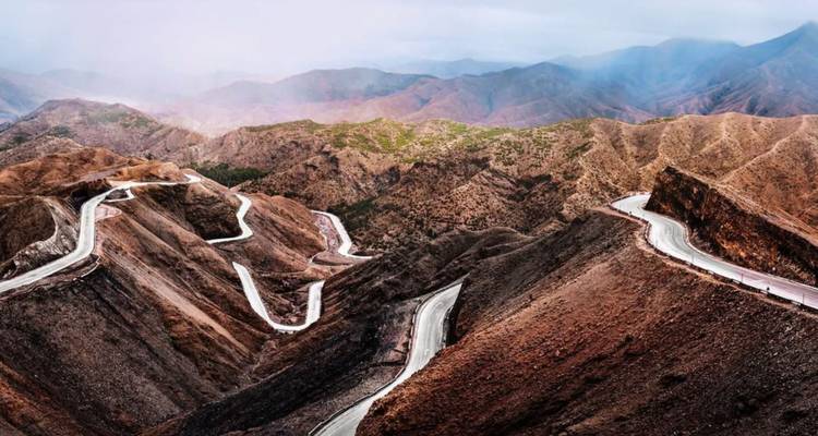 Winding mountain road snaking through rugged Atlas peaks under hazy sky