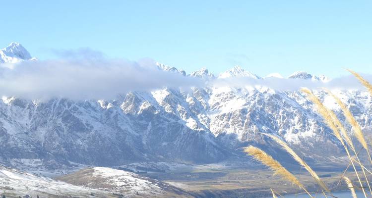 Snow-covered Remarkables mountain range with sweeping valley beneath low cloud.
