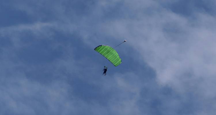 Green parachute canopy with solo skydiver descending against blue sky.