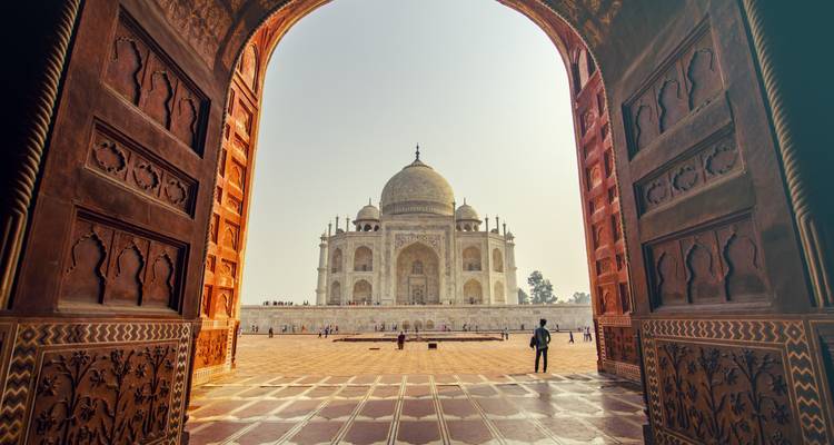 Majestuoso Taj Mahal enmarcado por la entrada ornamentada de una mezquita resplandeciendo en la suave bruma matutina.