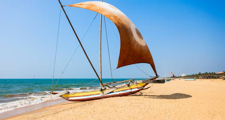 Traditionelles Auslegersegelkanu mit großem braunem Segel am sandigen Tropenstrand