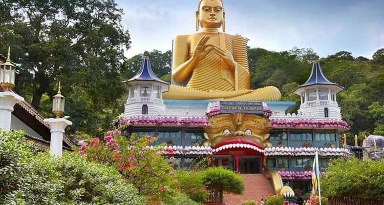Massive goldene Buddha-Statue thront über der kunstvollen Fassade des Dambulla Golden Temple inmitten von Grünzeug.