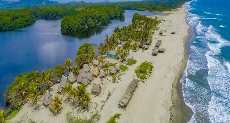 Luchtfoto van zandige kustlijn met met palmbladeren bedekte hutten en lagune