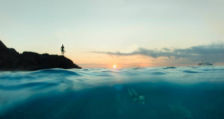Image à niveaux divisés d'un coucher de soleil sur la mer avec un plongeur en apnée sous la ligne de flottaison