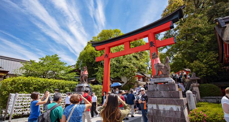 Menschenmengen, die durch das leuchtend rote Torii-Tor am Fushimi Inari-Schrein unter gestreiftem blauem Himmel hindurchgehen