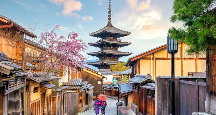 Schmale Holzgasse in Kyoto, die zur Yasaka-Pagode führt, mit Frühlingsblüten und Besuchern in Kimono