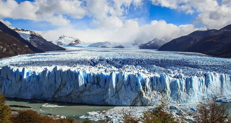 Massieve grillige ijsfront van de Perito Moreno Gletsjer die zich uitstrekt over melkachtig groene wateren onder een blauwe hemel.