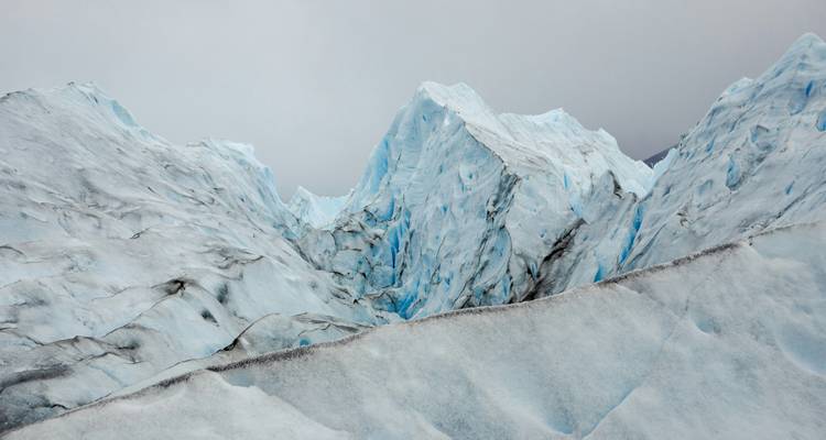 Abstrakte Nahaufnahme von scharfen schneebedeckten Gipfeln und Gletscherspalten auf einem patagonischen Gletscher unter grauem Himmel.