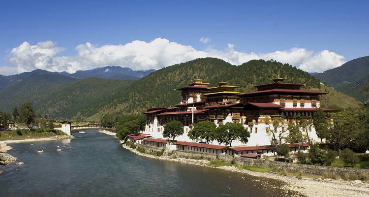 Elegant Punakha Dzong straddling the confluence of two rivers against a backdrop of forested Bhutanese mountains.