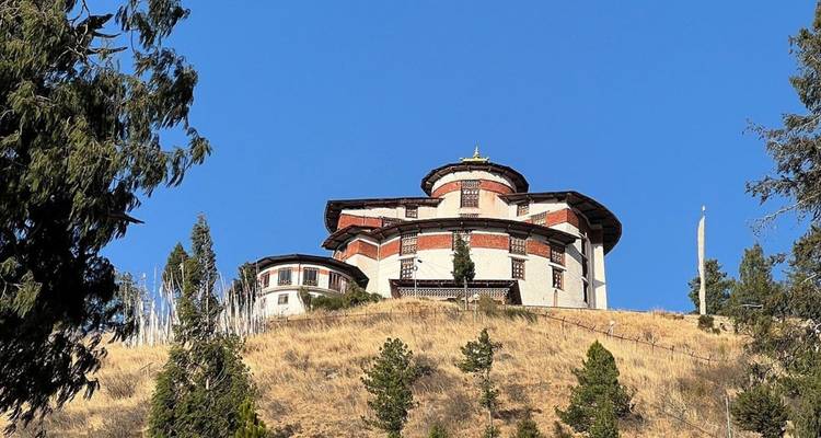 Round Bhutanese fortress-museum perched on a dry hillside under a clear blue sky.