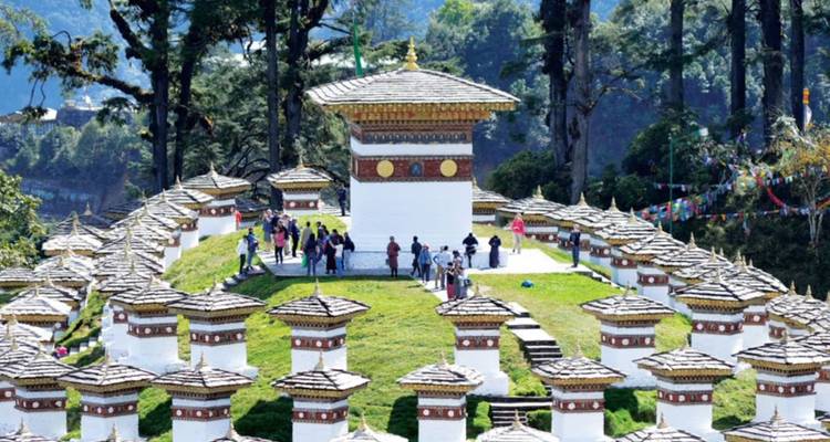 DochuLa Pass memorial chortens arranged in concentric rows on a grassy knoll with visitors walking among them.