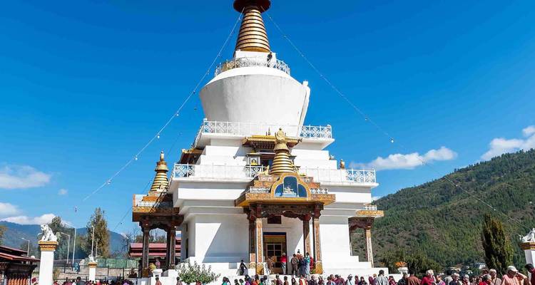 White Stupa-shaped Memorial Chorten in Thimphu surrounded by worshippers on a bright day.