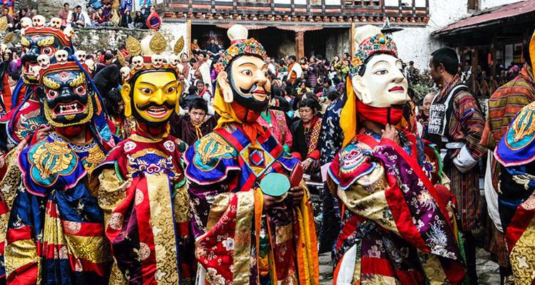 Vibrant masked dancers in elaborate costumes perform at a crowded Bhutanese religious festival.