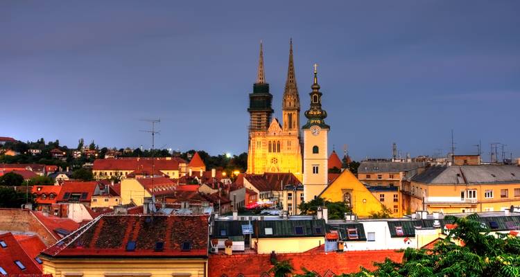 Abendhimmel von Zagreb mit beleuchteten Domtürmen, die sich über rotbedachte Gebäude erheben.