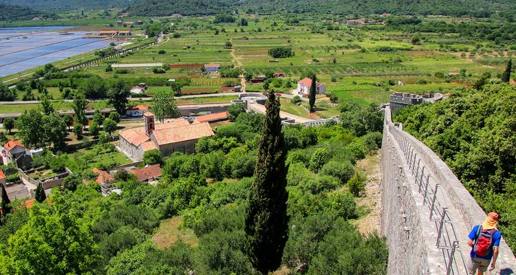Un excursionista solitario camina por las enormes murallas defensivas de piedra que dominan el campo verdoso y las salinas de Ston.