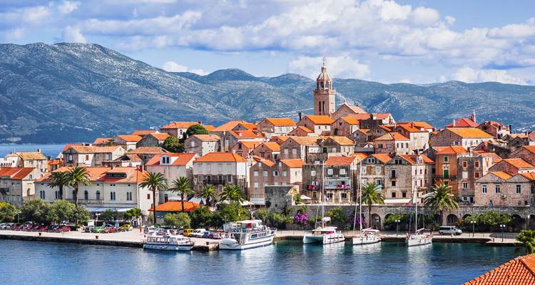 Schilderachtig uitzicht op de oude stad Korčula met terracotta daken en klokkentoren die uitsteken tegen een achtergrond van bergen en blauwe zee.