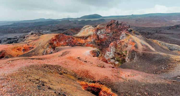 Cratères volcaniques colorés et champs de lave s'étendant sous un ciel couvert.