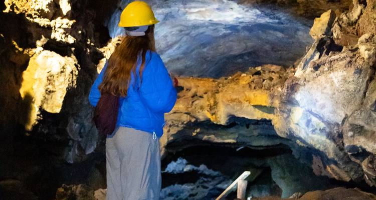 Visiteur portant un casque explore une grotte de tunnel de lave faiblement éclairée avec une lampe torche.