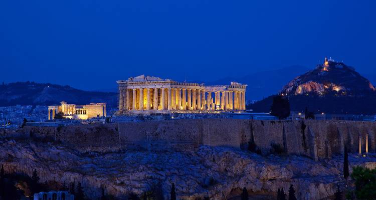De verlichte Parthenon domineert de skyline van Athene tegen een diepblauwe nachtelijke hemel.