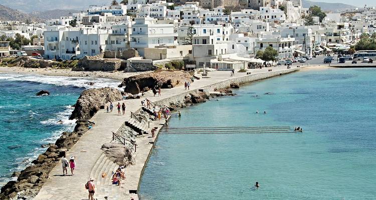 Paseo junto al mar y nadadores junto al pueblo blanqueado de Naxos con agua turquesa