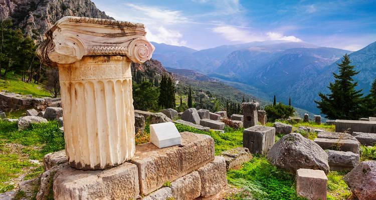Fragment de colonne antique à Delphes encadré par des chaînes de montagnes lointaines et des arbres à feuilles persistantes.