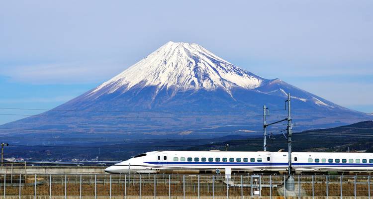 Un shinkansen passe à toute vitesse devant le mont Fuji enneigé sous un ciel bleu dégagé.