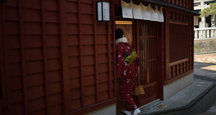 Person in Blumenkimono, die in eine traditionelle Teehausgasse mit Holzbauweise tritt