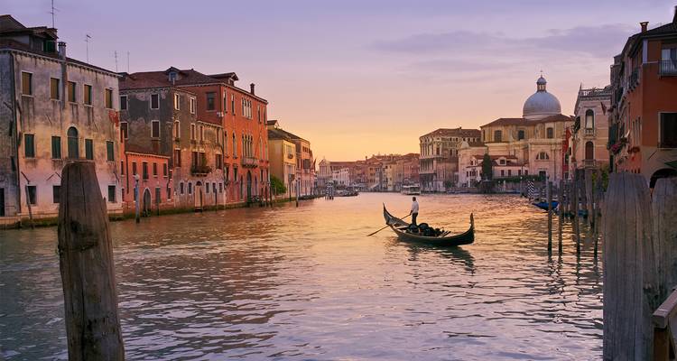 A gondolier rows down Venice’s Grand Canal at golden sunset, buildings glowing on either side.
