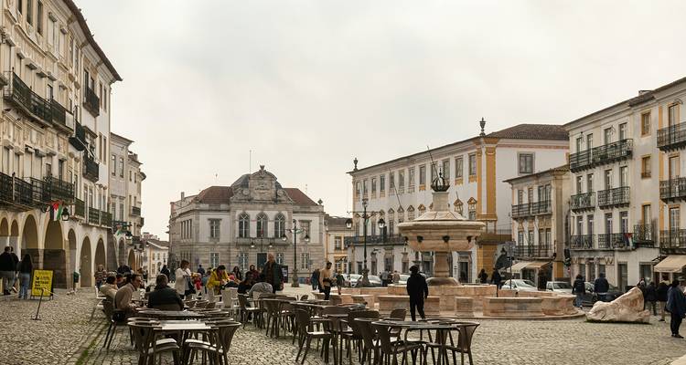 Plaza empedrada bordeada de cafés con fuente central en la histórica ciudad de Évora.