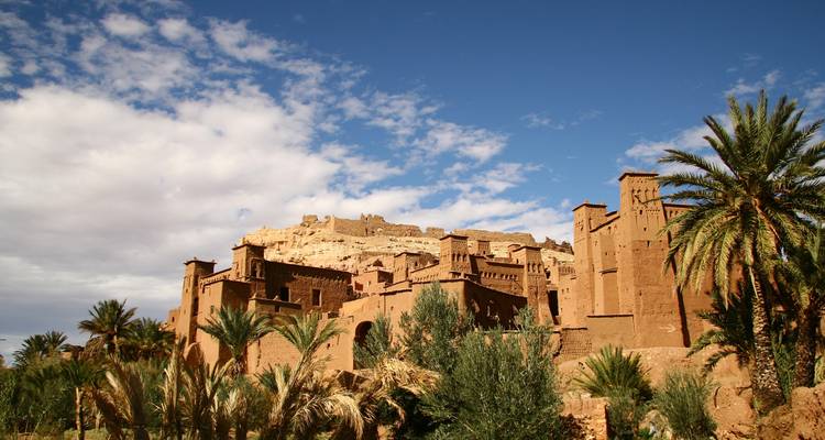 Las palmeras enmarcan las murallas del ksar en la cima de la colina de Ait Benhaddou contra un cielo azul brillante.