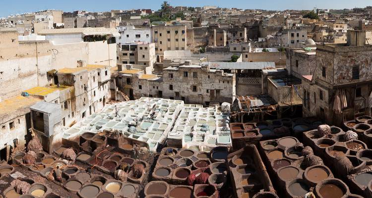 Vista panorámica de las antiguas curtidurías de cuero de Fez con cubas de tintes vibrantes y edificios de piedra circundantes.