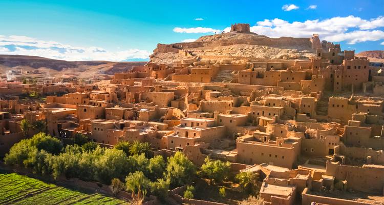 Les anciennes casbahs de terre d'Ait Benhaddou s'élèvent au-dessus d'une oasis luxuriante sous un ciel bleu.