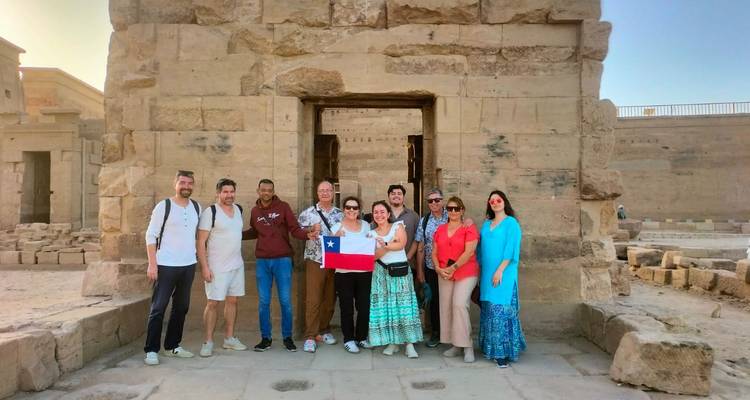 Grupo de turistas posando con bandera frente a la entrada de un templo de piedra antiguo
