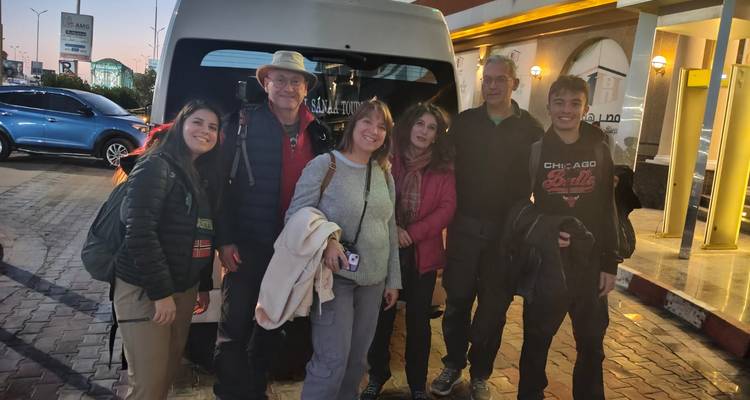 Pequeño grupo turístico de pie junto a una minivan por la noche fuera de un edificio