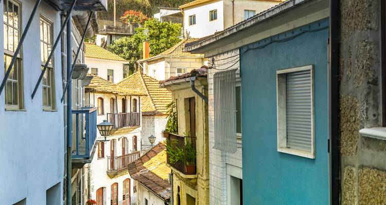 Pintoresca calle estrecha bordeada de casas de colores pastel y jardineras con flores en un pequeño pueblo portugués.