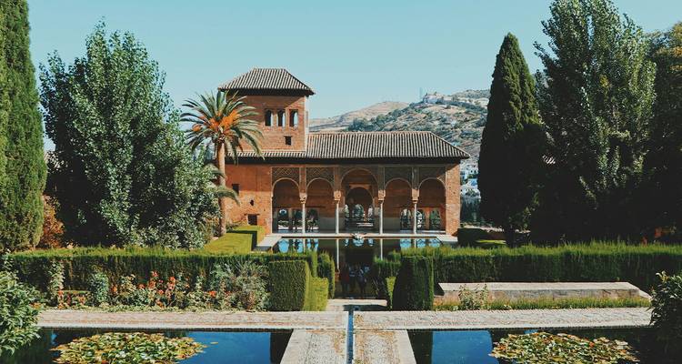 Serene garden courtyard of the Alhambra with reflective pools, cypress trees and Moorish arches.