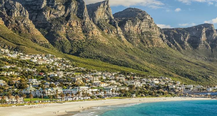Aerial view of Cape Town’s Camps Bay with Twelve Apostles mountains towering above seaside suburb.